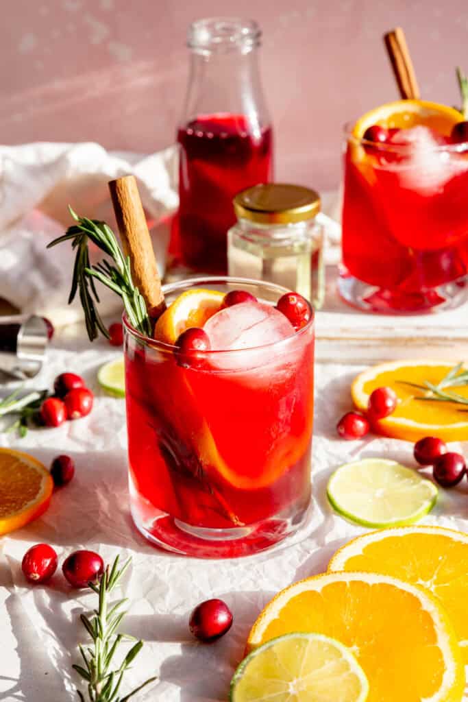 Two cranberry margaritas, a jar of simple syrup and a jug of cranberry juice.