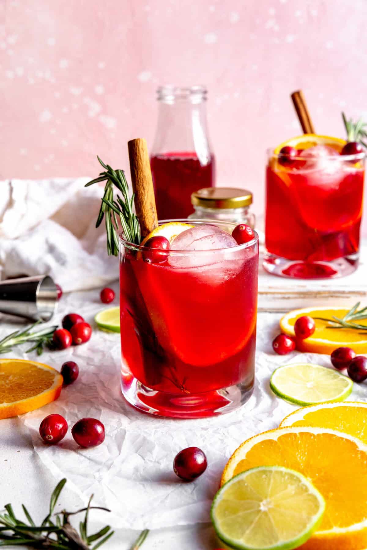 Two cranberry margaritas, a jug of cranberry juice and orange slices.