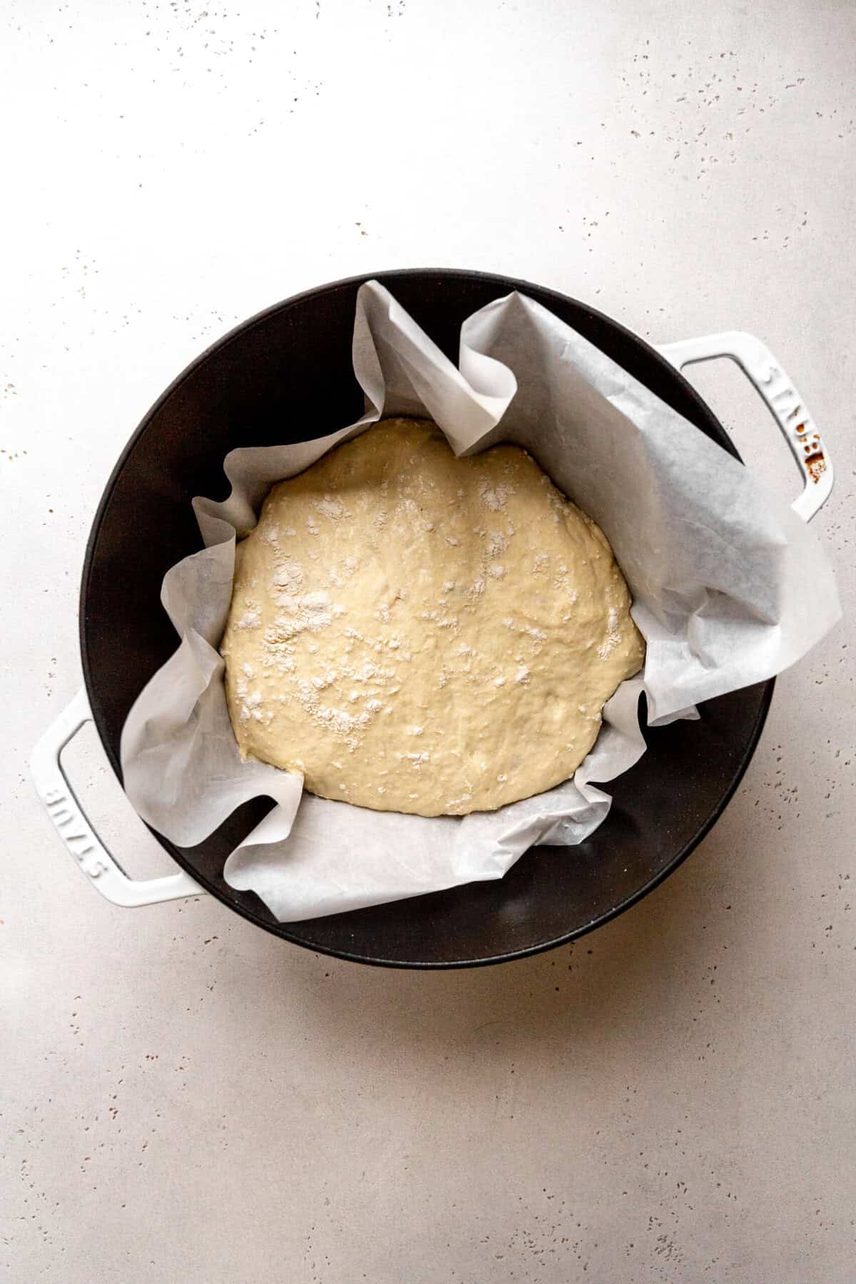Unbaked bread dough in a dutch oven lined with parchment paper.