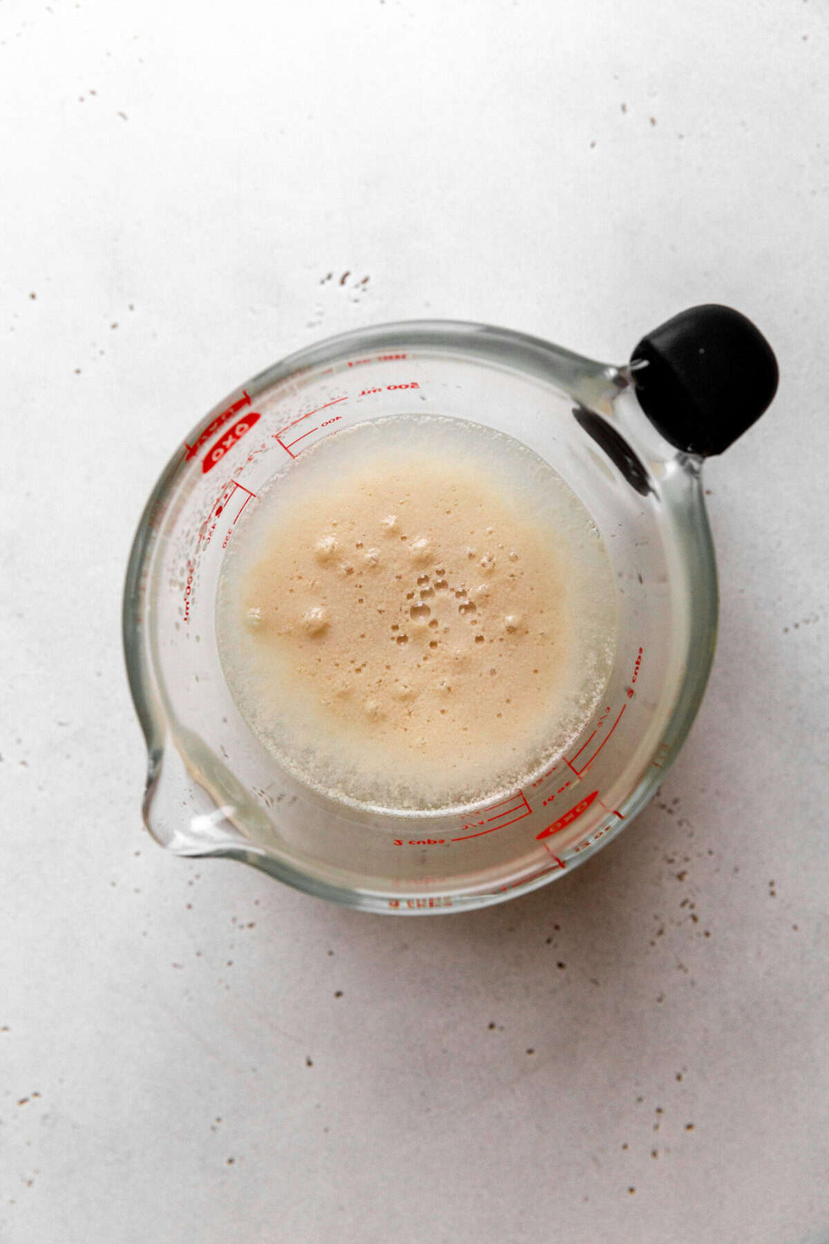 Measuring cup filled with water, sugar and yeast.