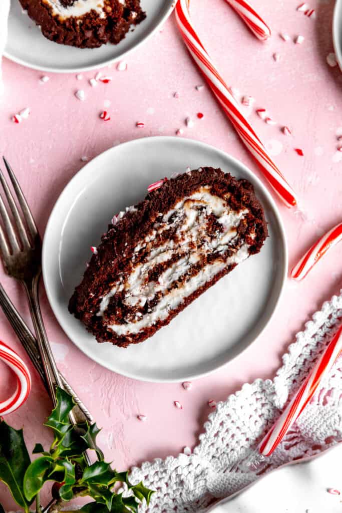 Slice of chocolate peppermint tule log cake on a white plate surrounded by candy canes.