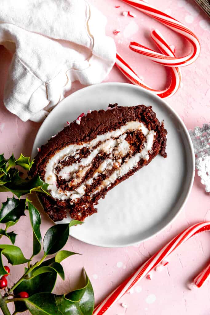 Slice of chocolate peppermint tule log cake on a white plate surrounded by candy canes.