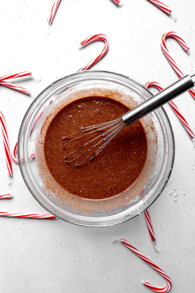 Glass bowl of chocolate cake batter with a whisk surrounded by candy canes.