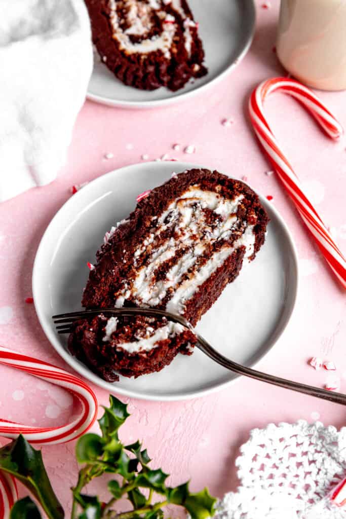 Fork cutting into a slice of chocolate peppermint yule log cake surrounded by candy canes.