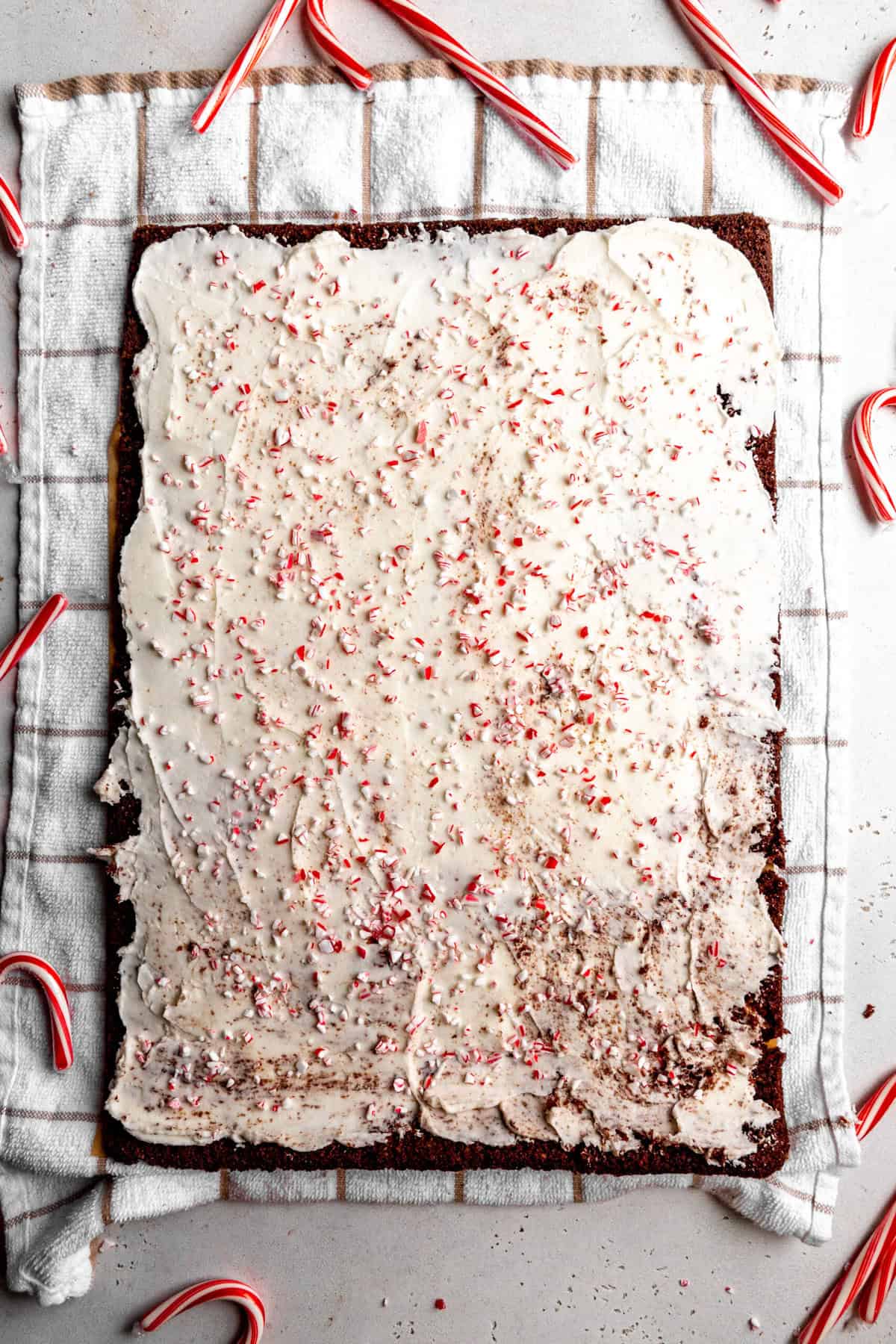 Chocolate cake lying on a towel topped with frosting and crushed candy canes.