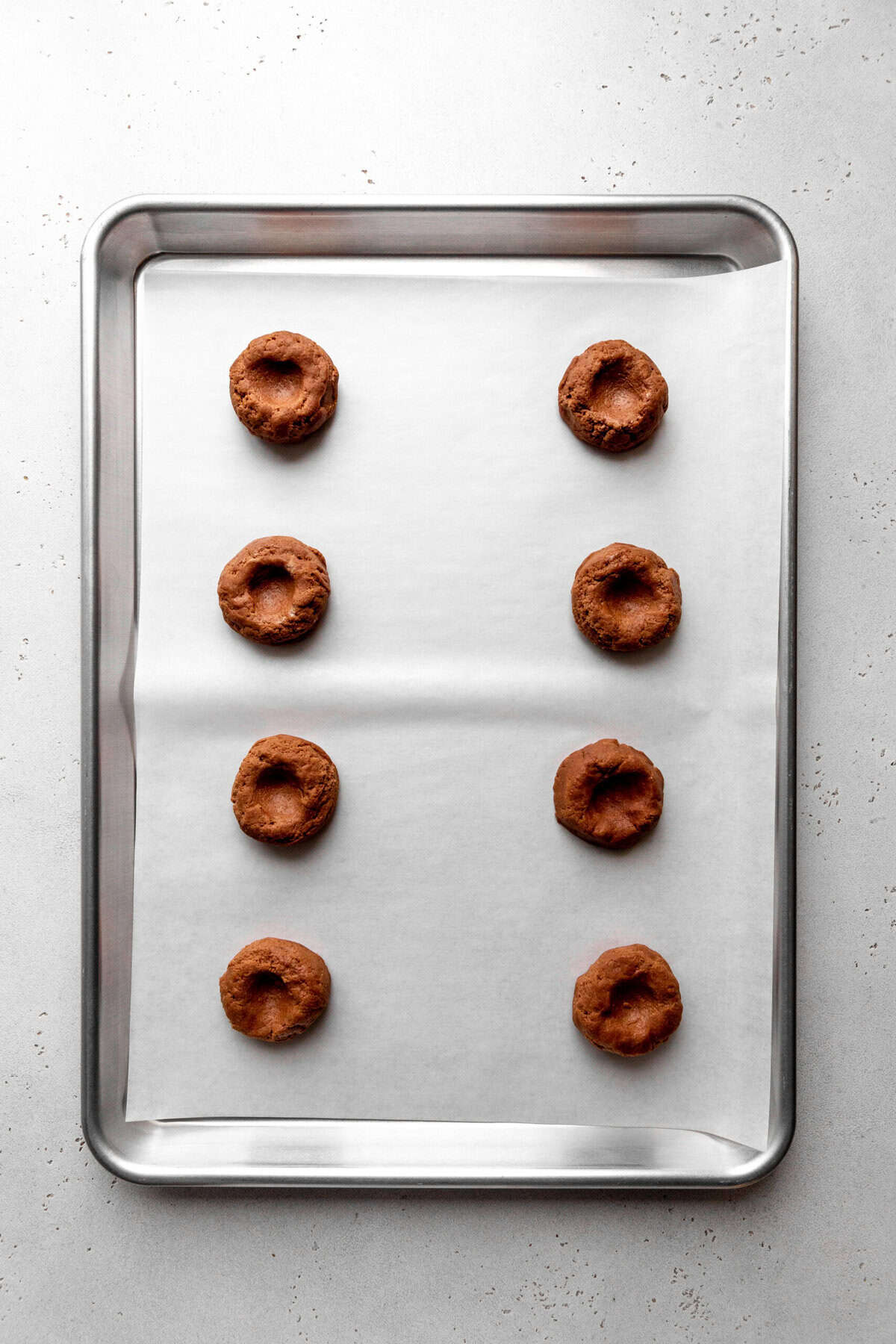 Unbaked chocolate thumbprint cookies on a baking sheet.