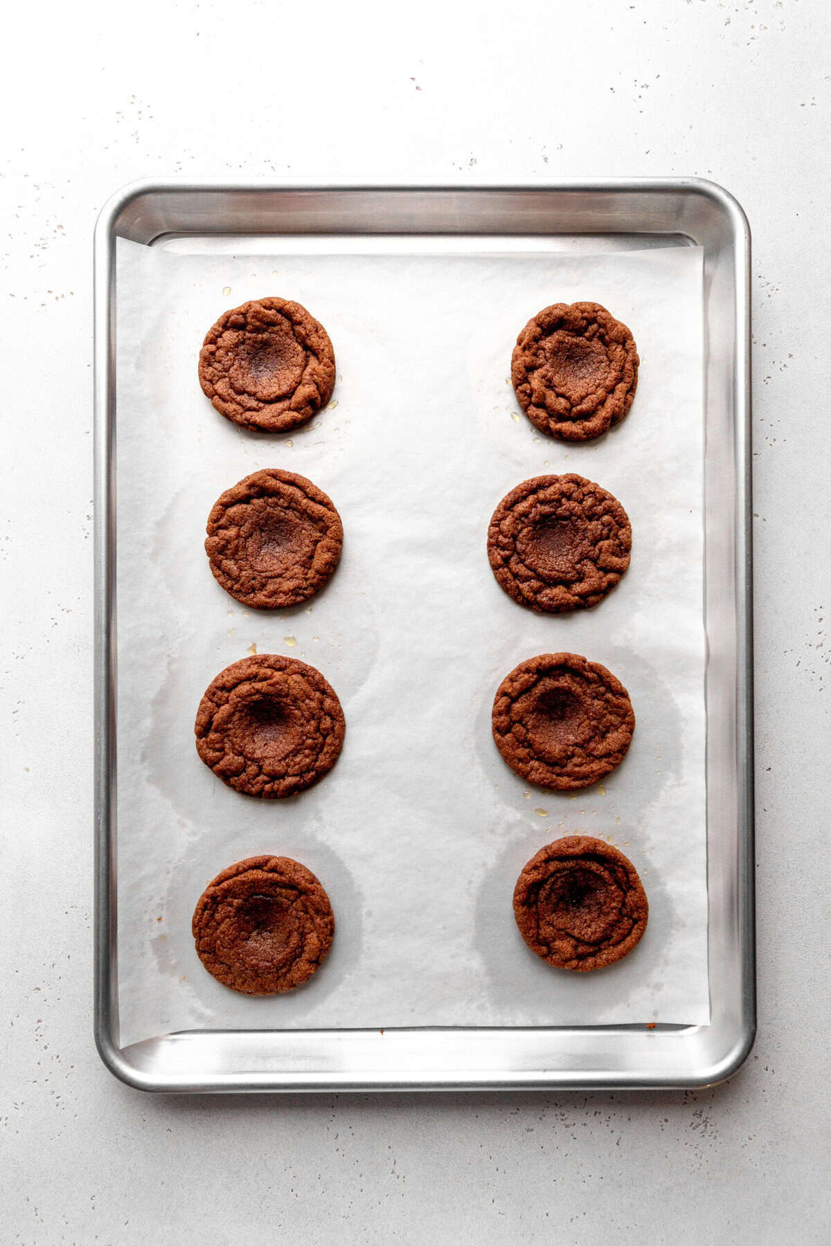 Baked chocolate thumbprint cookies on a baking sheet.