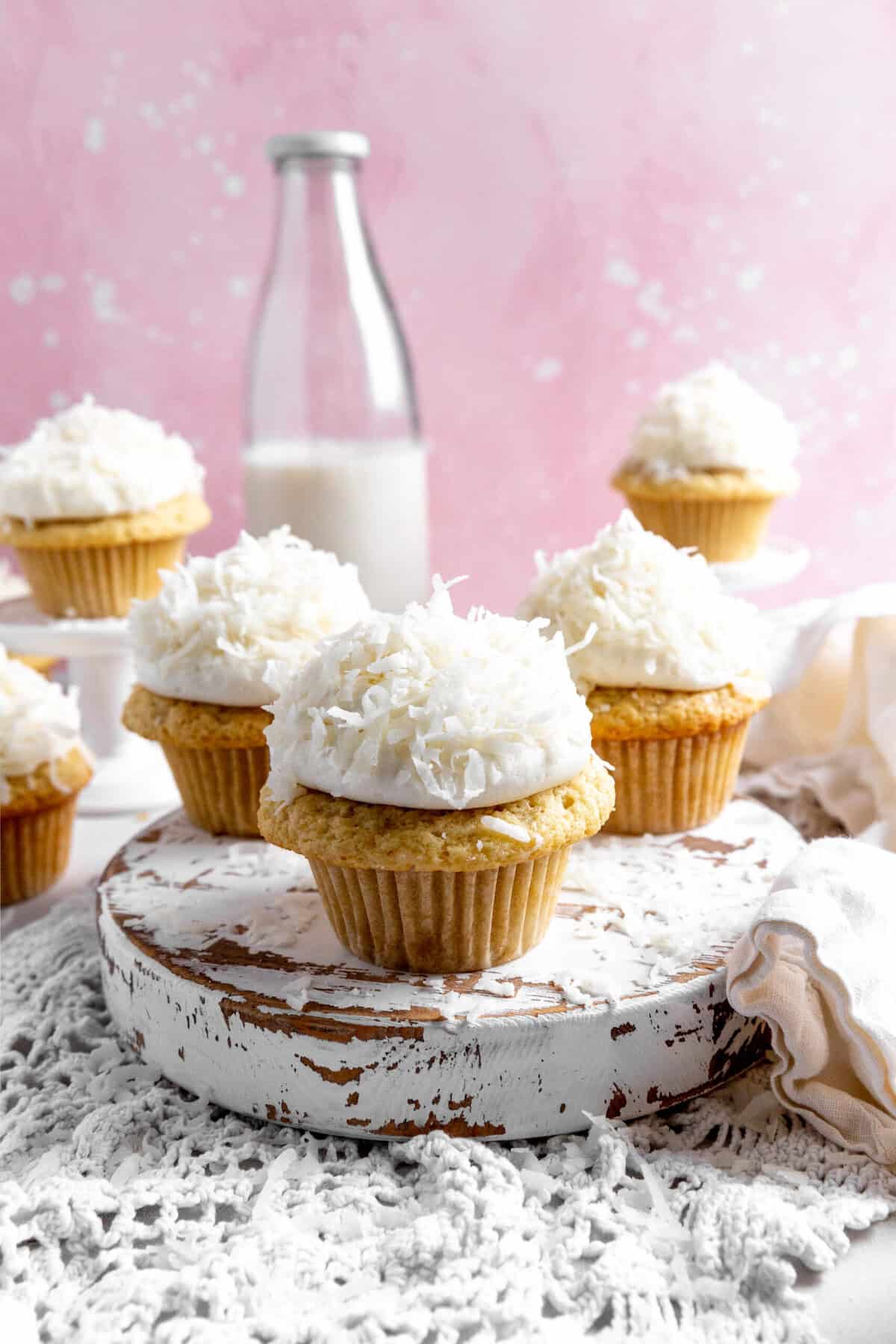 Coconut cream cupcakes on a wooden platter and a jug of milk.