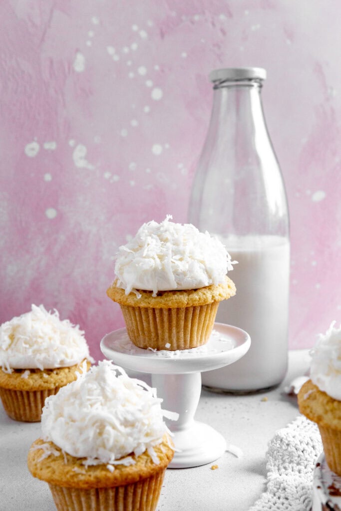 Coconut cupcake on a pedestal and a jug of milk.