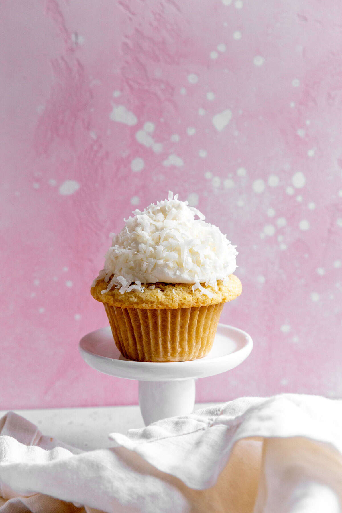 Coconut cream cupcake on a pedestal and a white linen napkin.
