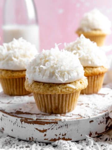 Coconut cream cupcakes on a white, wooden platter.