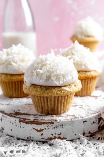 Coconut cream cupcakes on a white, wooden platter.