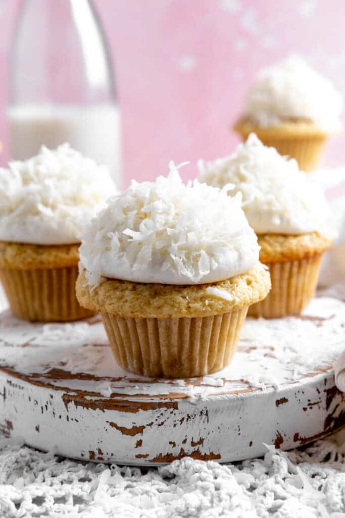Coconut cream cupcakes on a white, wooden platter.