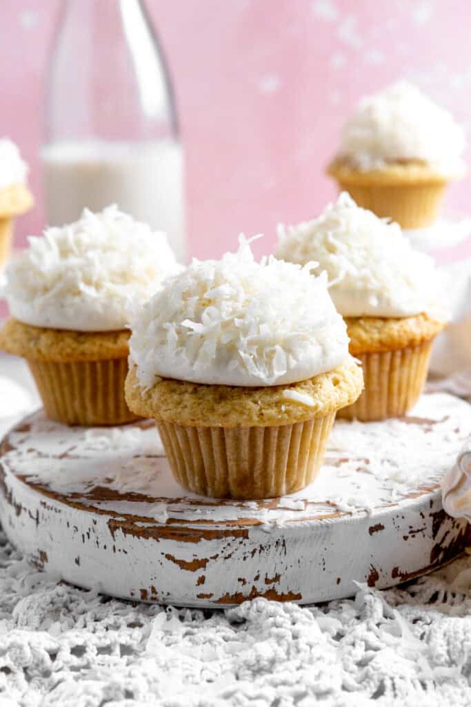 Coconut cream cupcakes on a white, wooden platter.