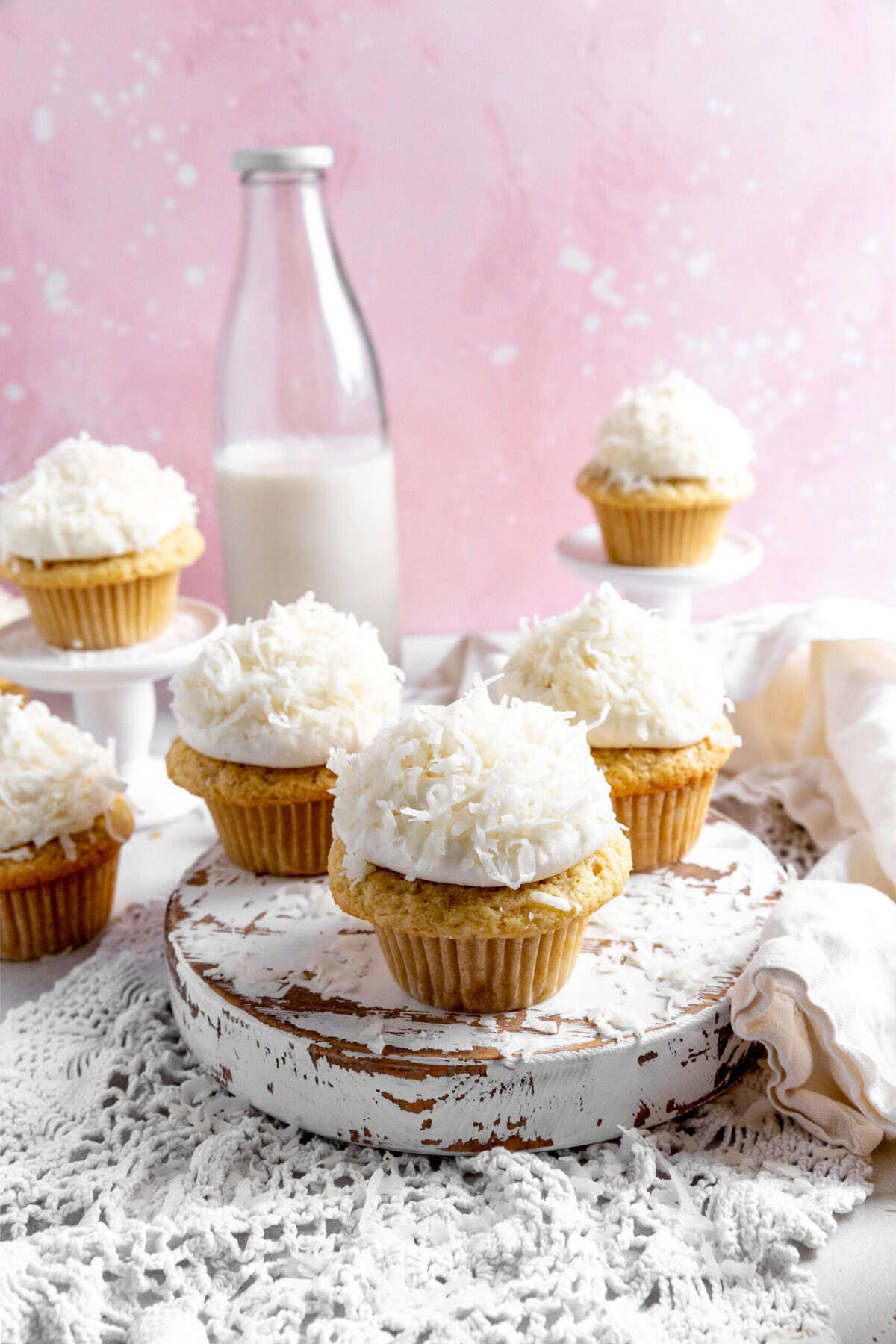 Coconut cream cupcakes on a wooden platter and a jug of milk.