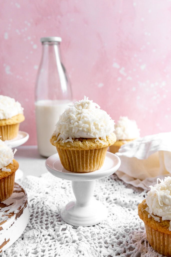 Coconut cream cupcake on a pedestal and a jug of milk.