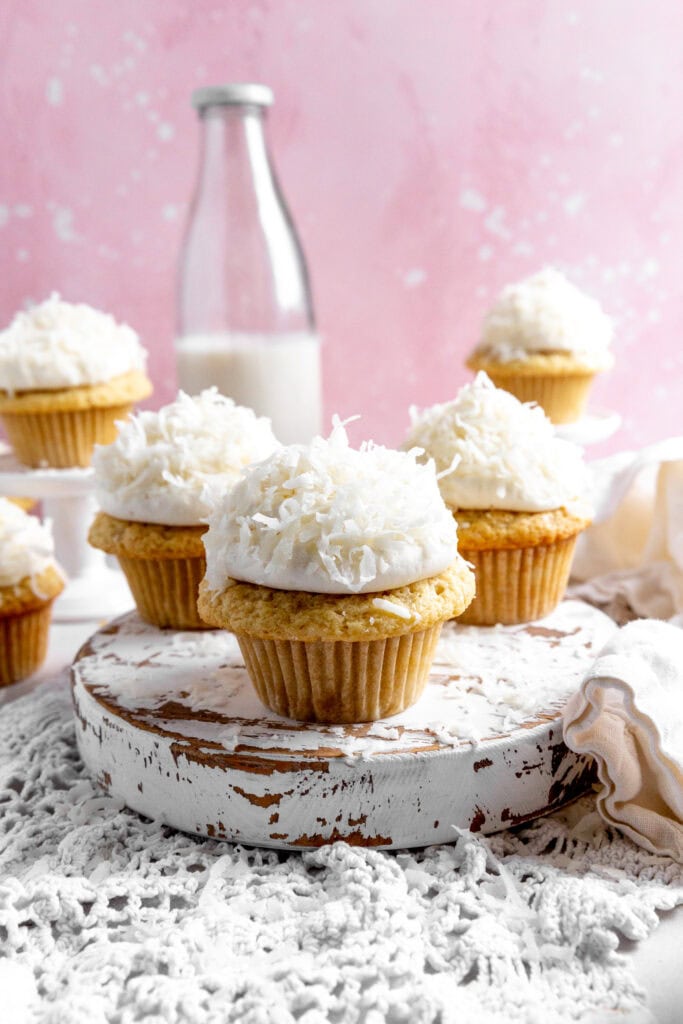 Coconut cream cupcakes on a wooden platter and a jug of milk.