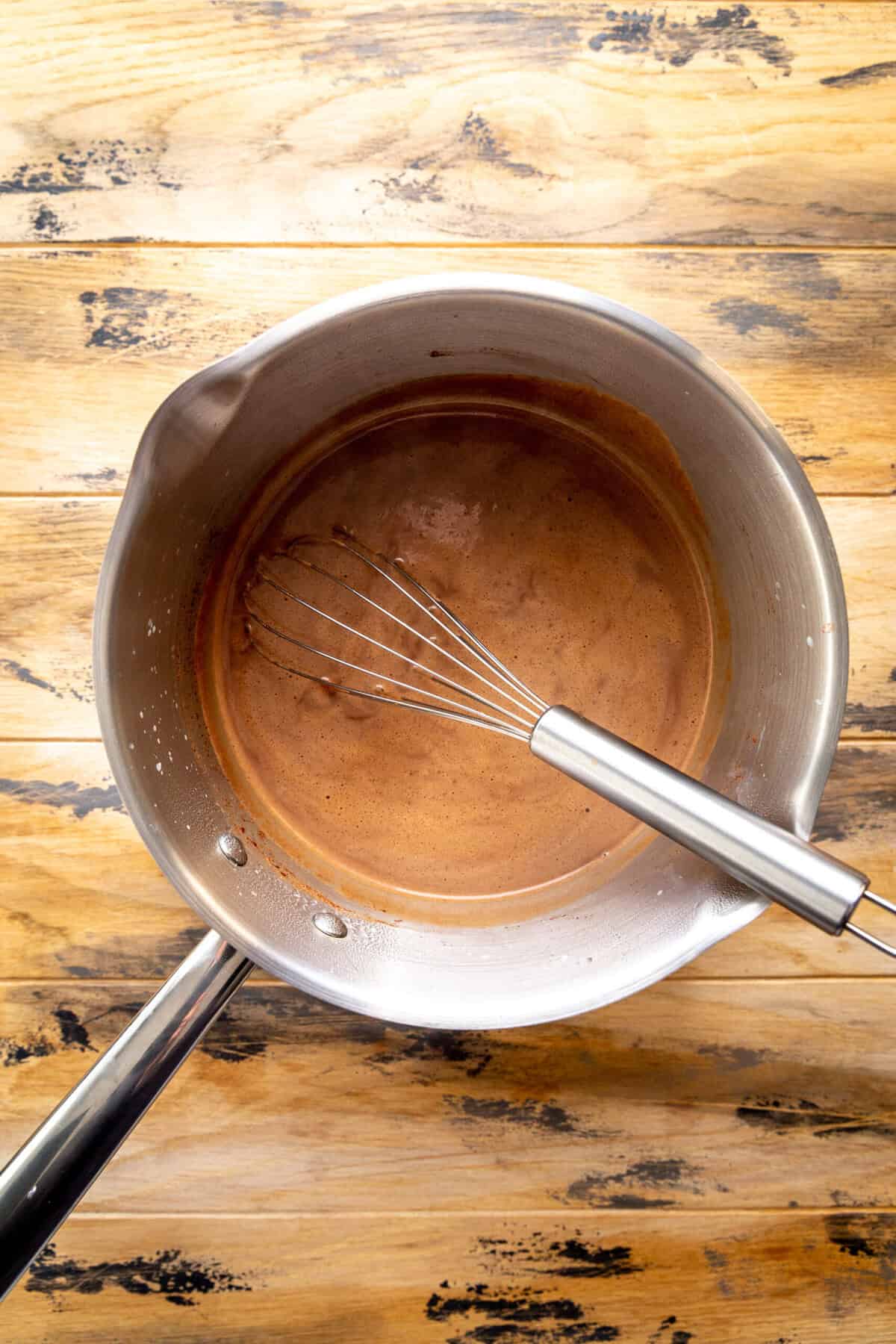 Hot chocolate in a saucepan with a whisk.