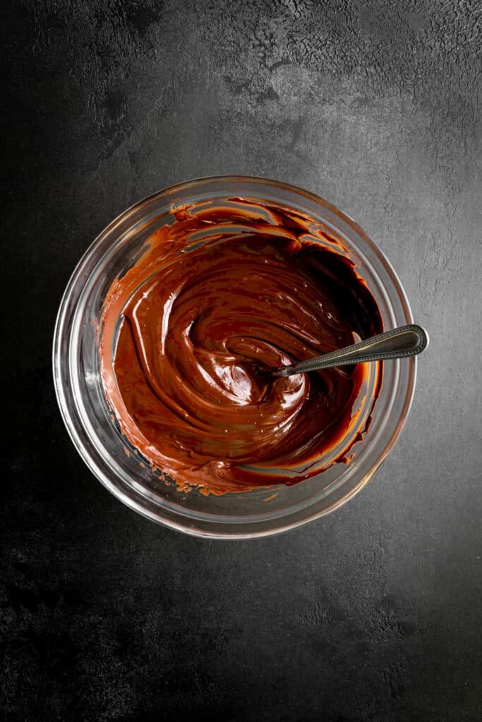 Glass bowl of melted chocolate with a spoon.