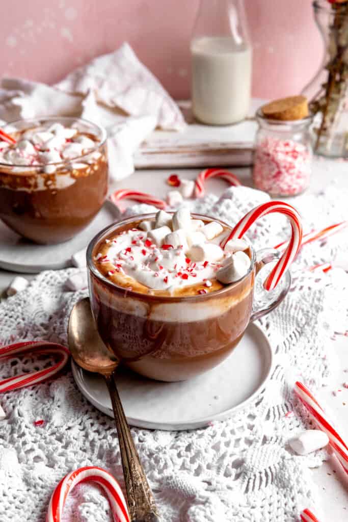 Two mug of peppermint hot chocolate topped with whipped cream, marshmallows and candy canes.