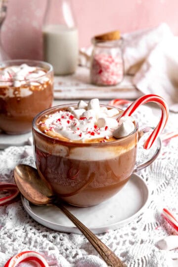 Mug of peppermint hot chocolate, jug of milk, and a jar of crushed candy canes.