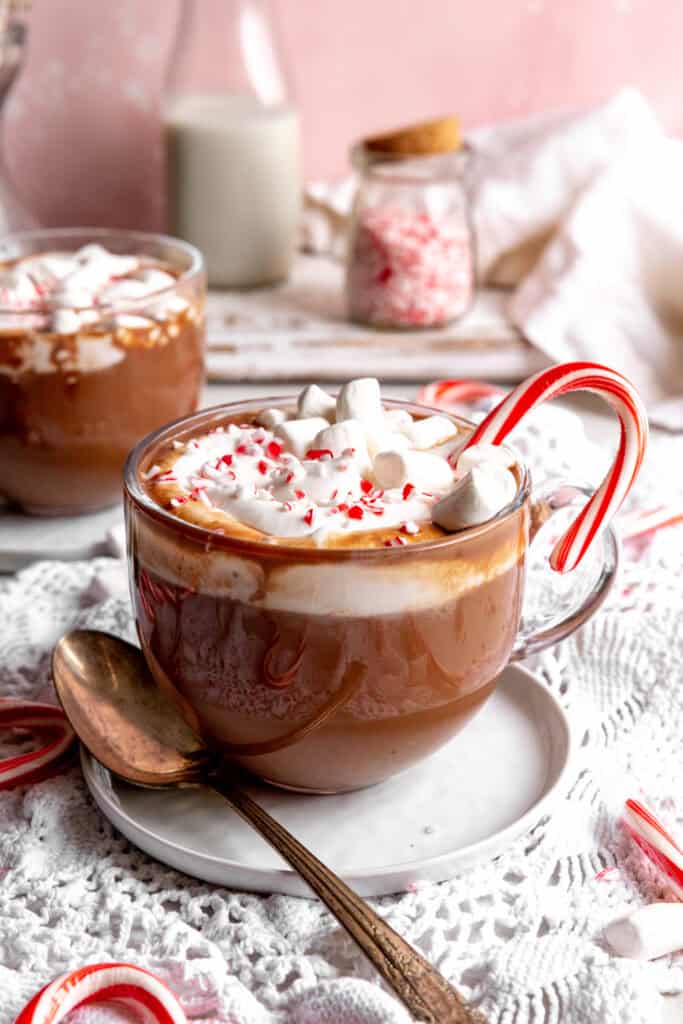 Mug of peppermint hot chocolate, jug of milk, and a jar of crushed candy canes.
