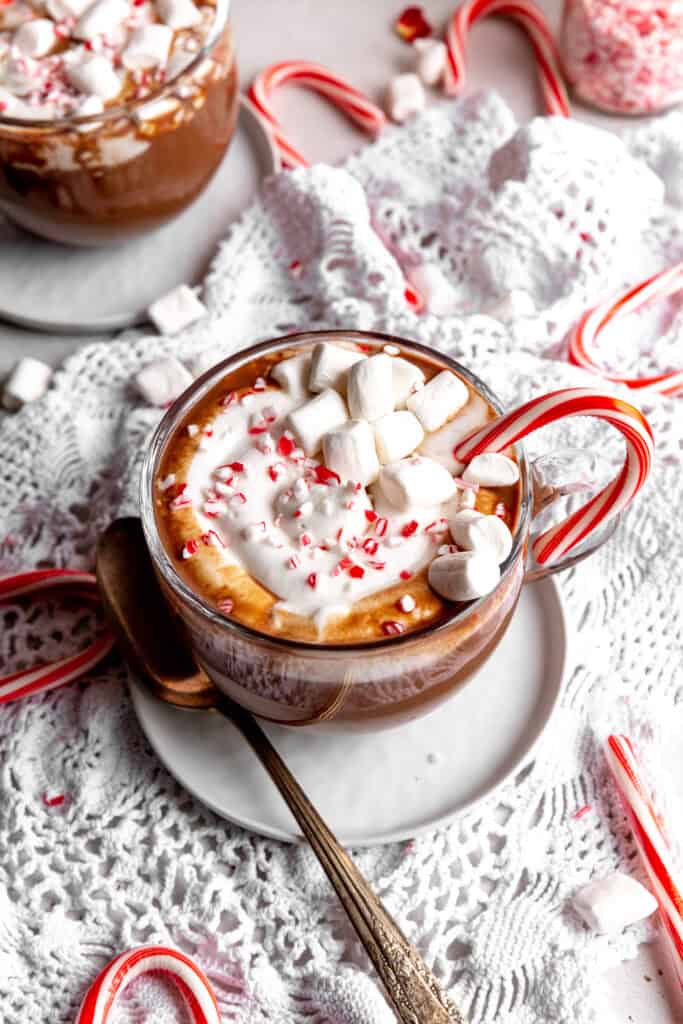 Mug of peppermint hot chocolate with a candy cane on a white plate with a spoon.