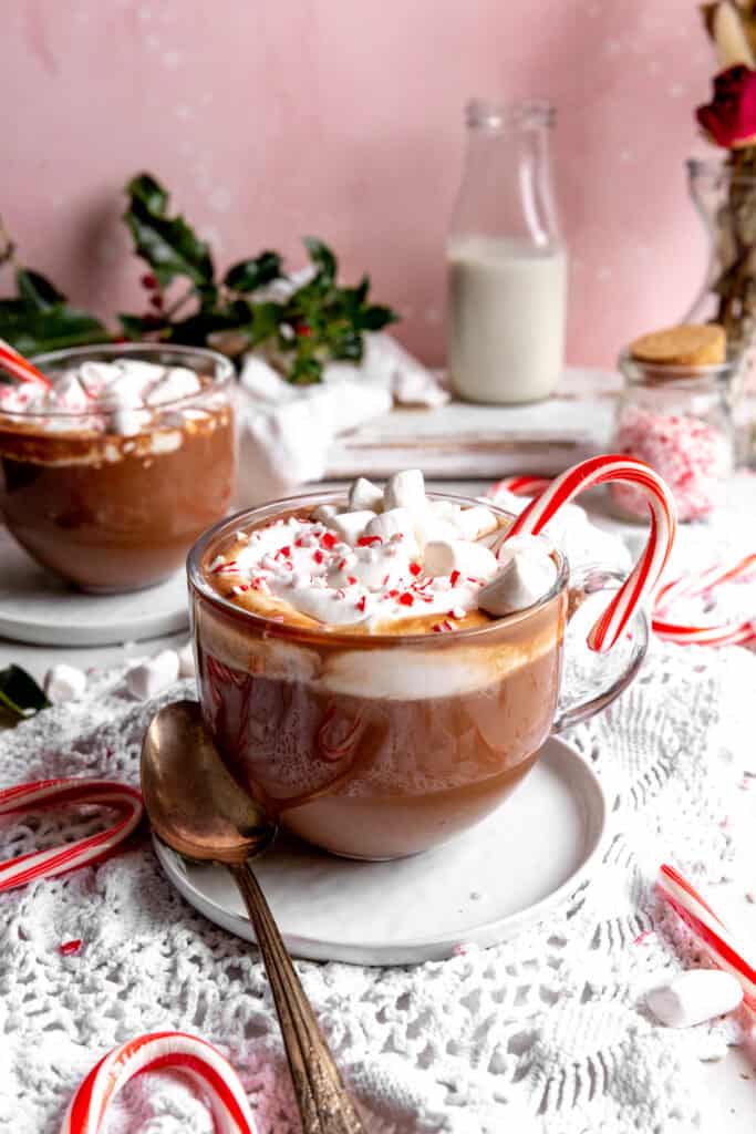 Two mugs of peppermint hot chocolate, a jug of milk and a jar of crushed candy canes.