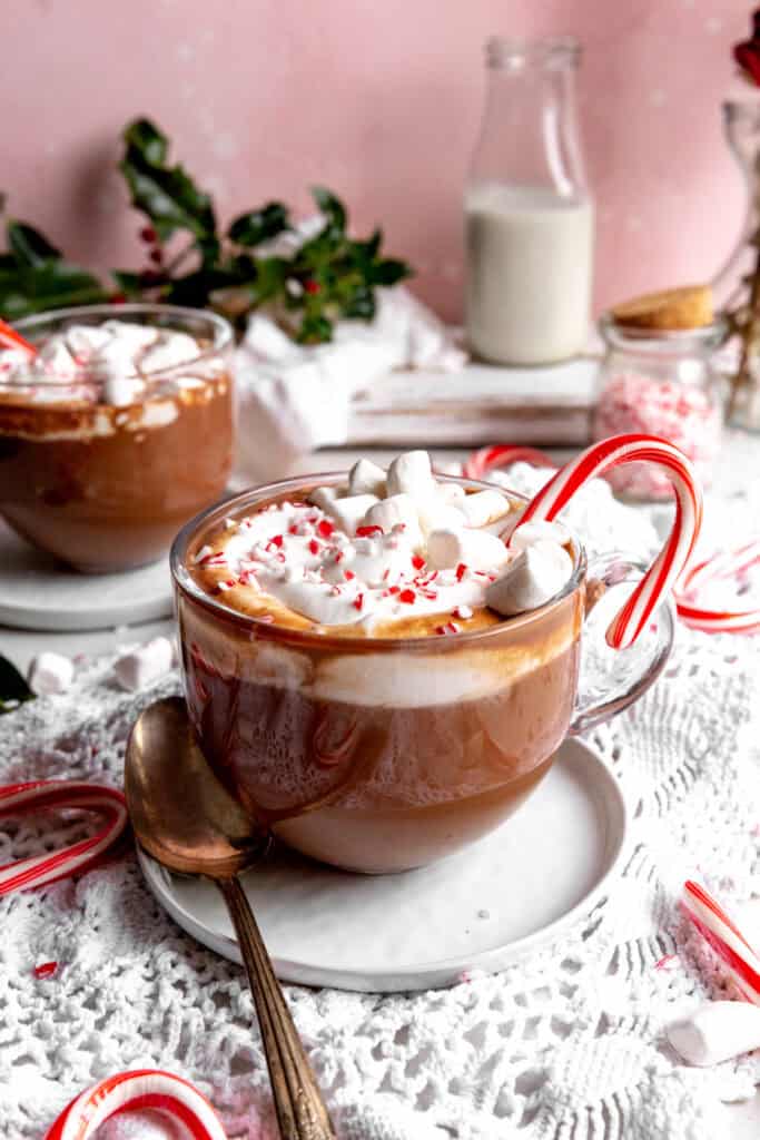 Two mugs of peppermint hot chocolate, a jug of milk and a jar of crushed candy canes.