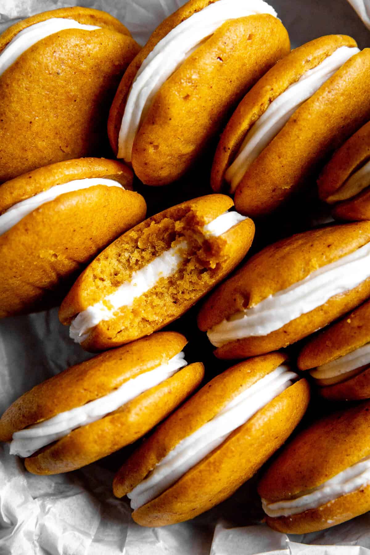 Pumpkin whoopie pie with a bite taken out of it in a tray with more whoopie pies.