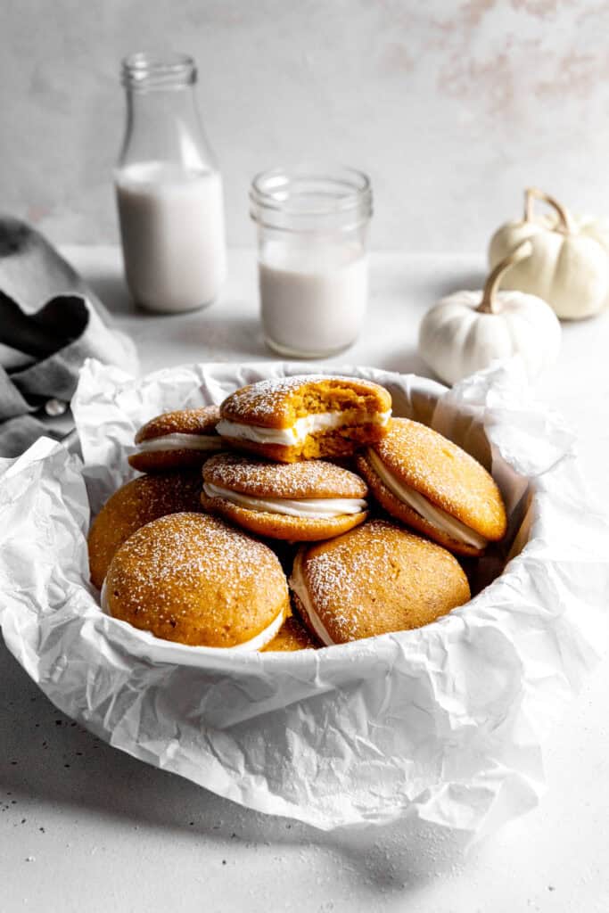 Pumpkin whoopie pie with a bite taken out of it in a bowl of more whoopie pies.