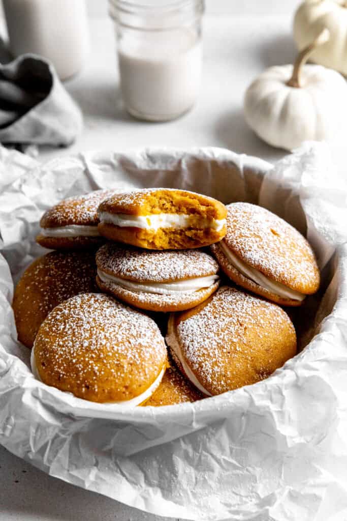 Pumpkin whoopie pie with a bite taken out of it in a bowl of more whoopie pies.