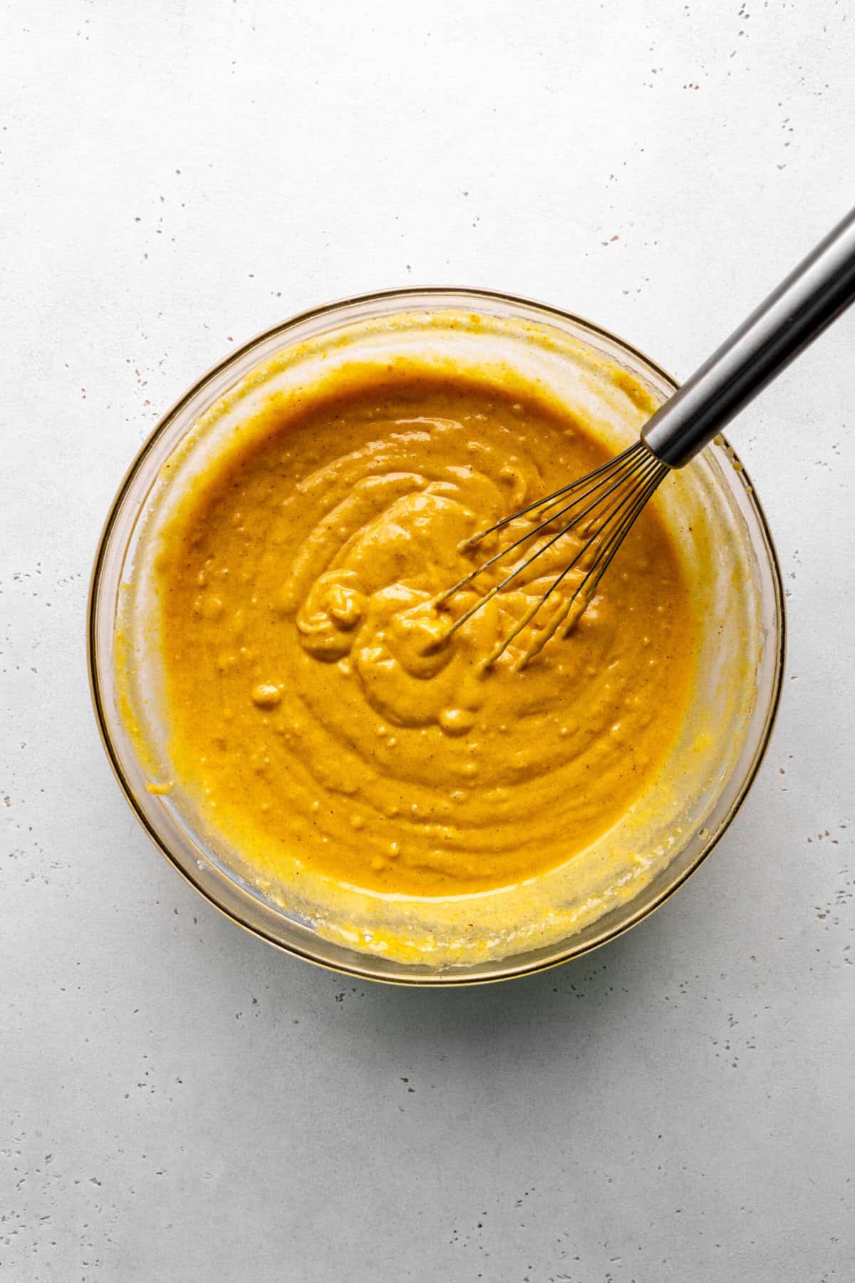 Glass bowl of pumpkin cake batter and a wire whisk.