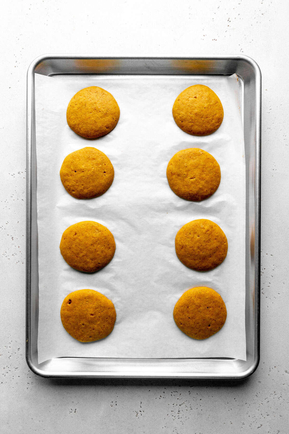 Baked pumpkin whoopie pies on a baking sheet.