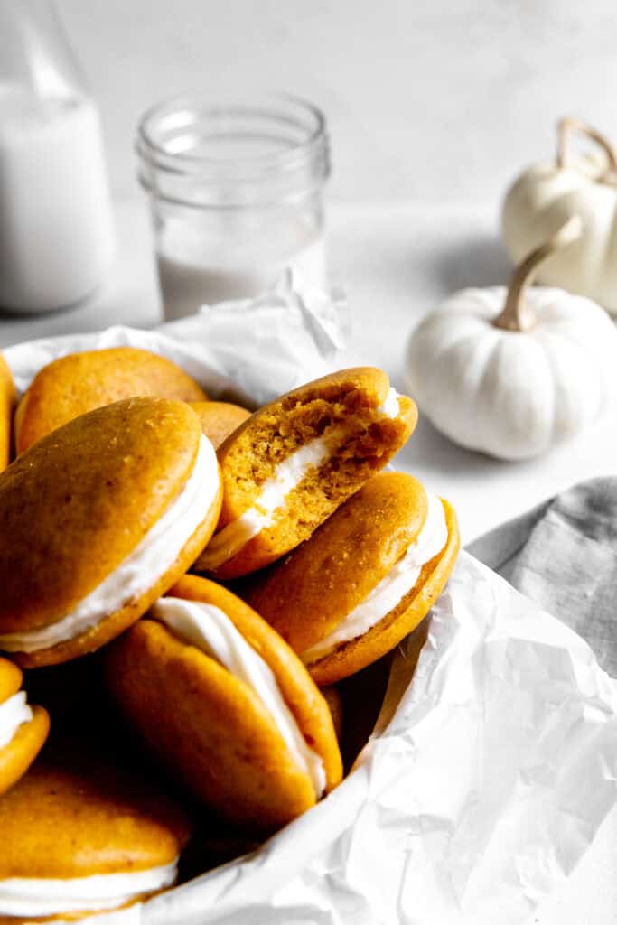 Pumpkin whoopie pie with a bite missing, two white pumpkins and a glass of milk.