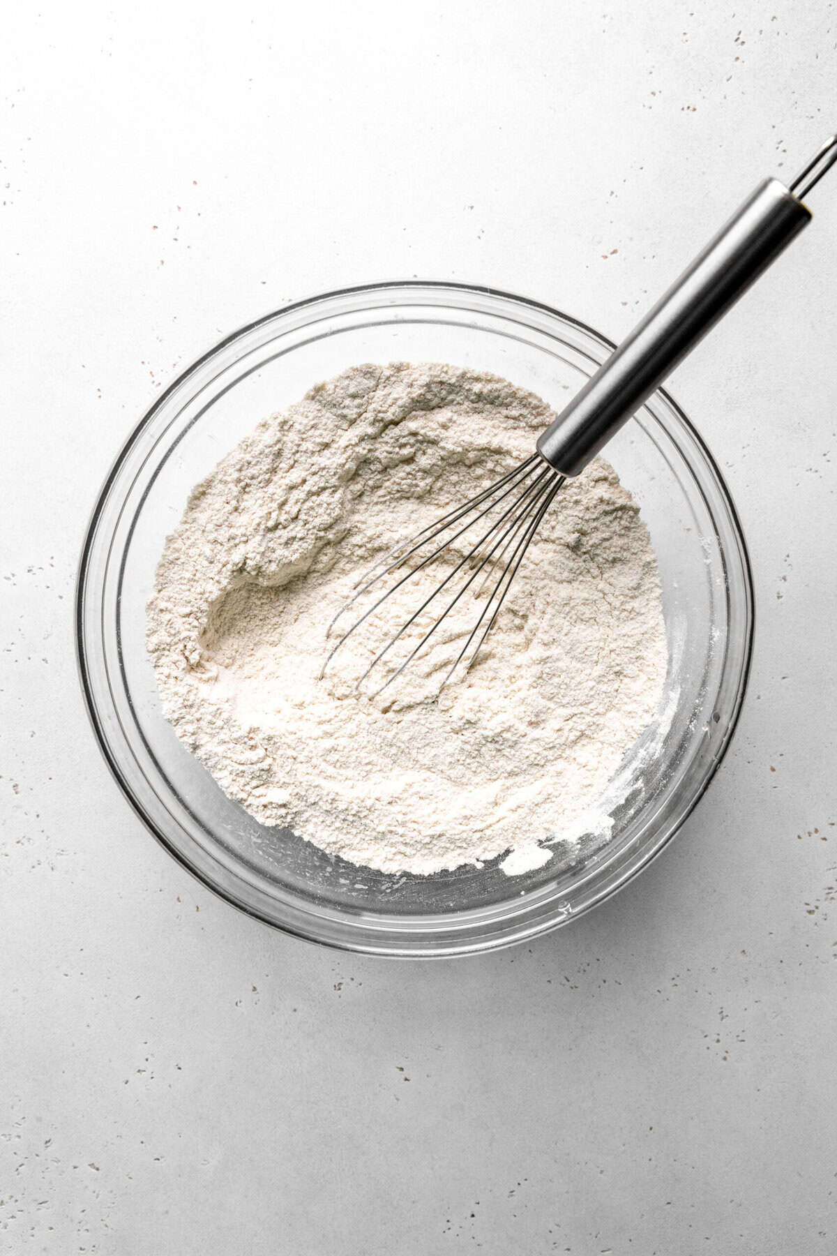 Glass bowl filled with flour and a wire whisk.