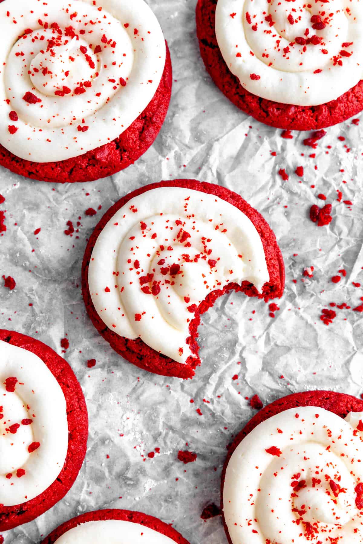 Red velvet cake cookie with a bite taken out of it and scattered cookie crumbs.