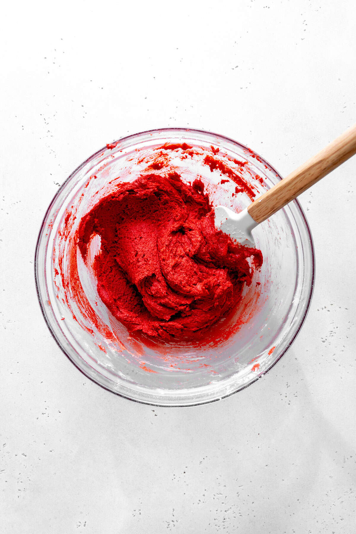 Glass bowl of red velvet cookie dough and a rubber spatula.