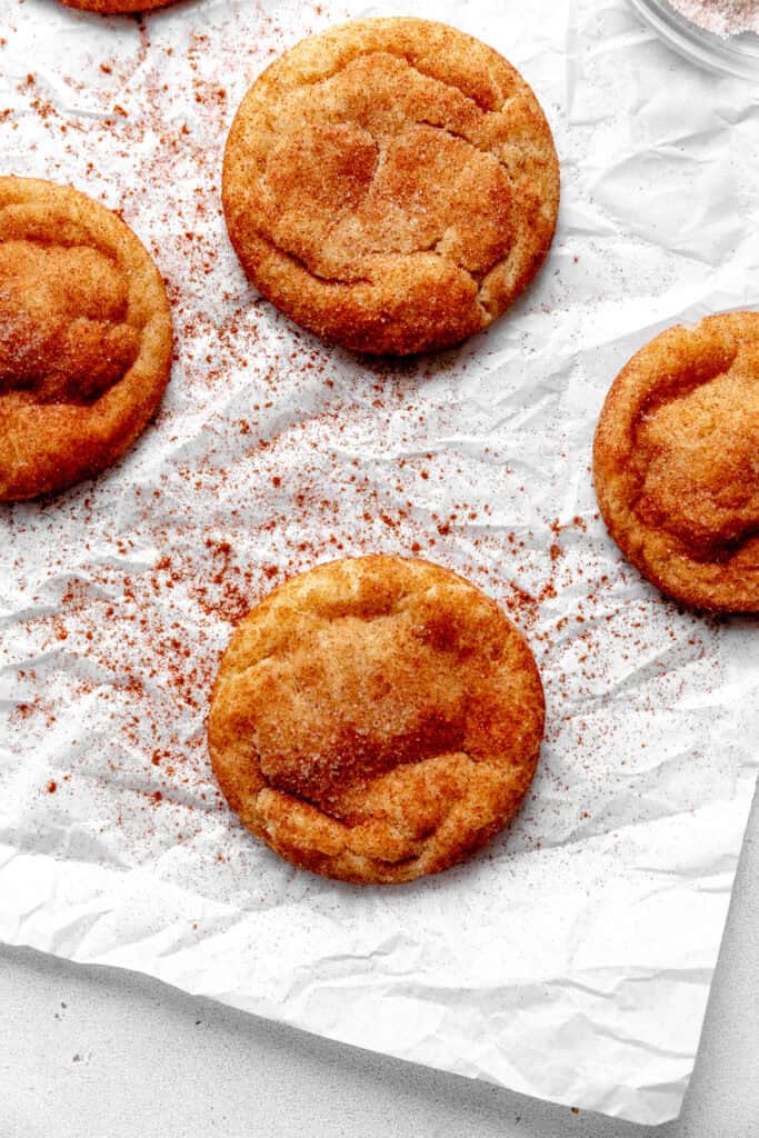 Vegan snickerdoodles on parchment paper sprinkled with cinnamon.