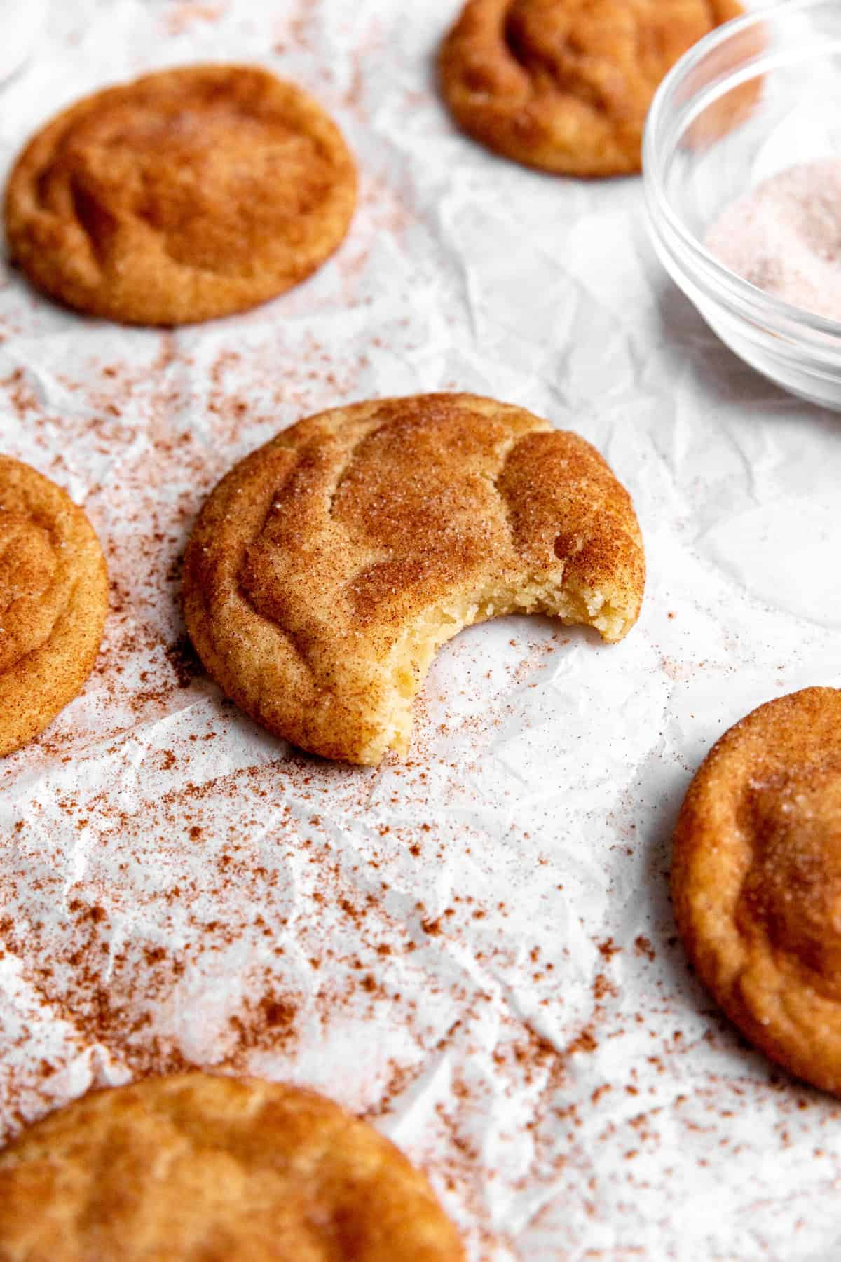 Snickerdoodle cookie with a bite taken out of it and a bowl of cinnamon-sugar.