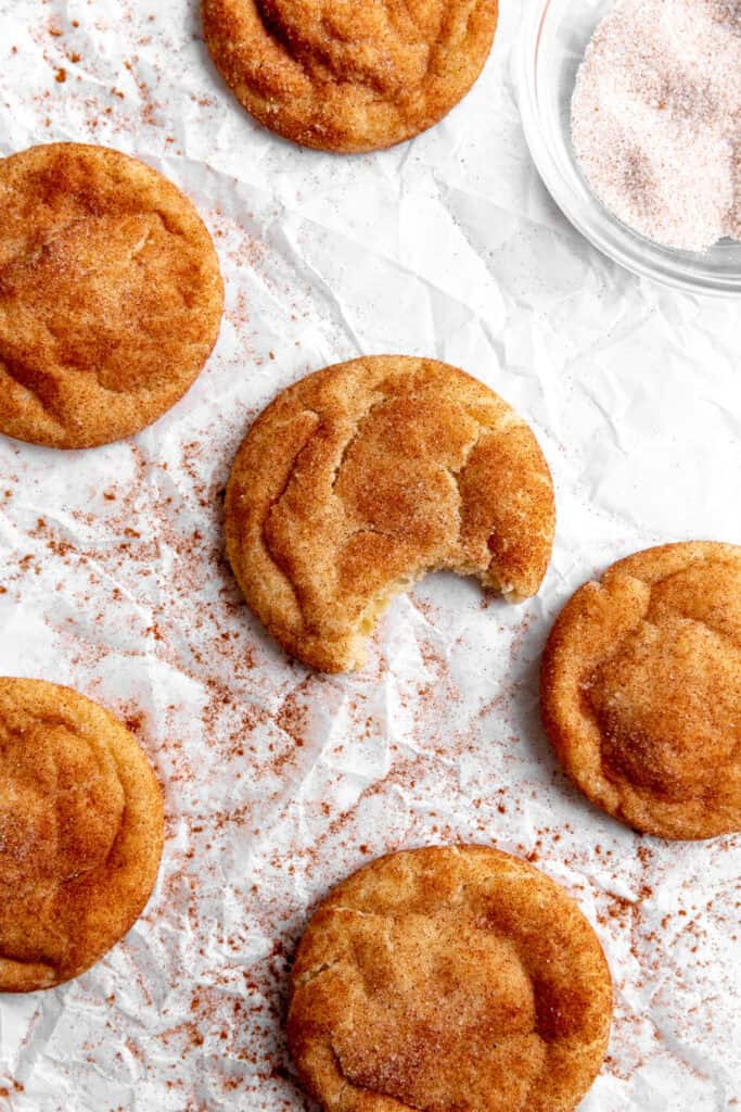 Snickerdoodle cookie with a bite taken out of it and a bowl of cinnamon-sugar.