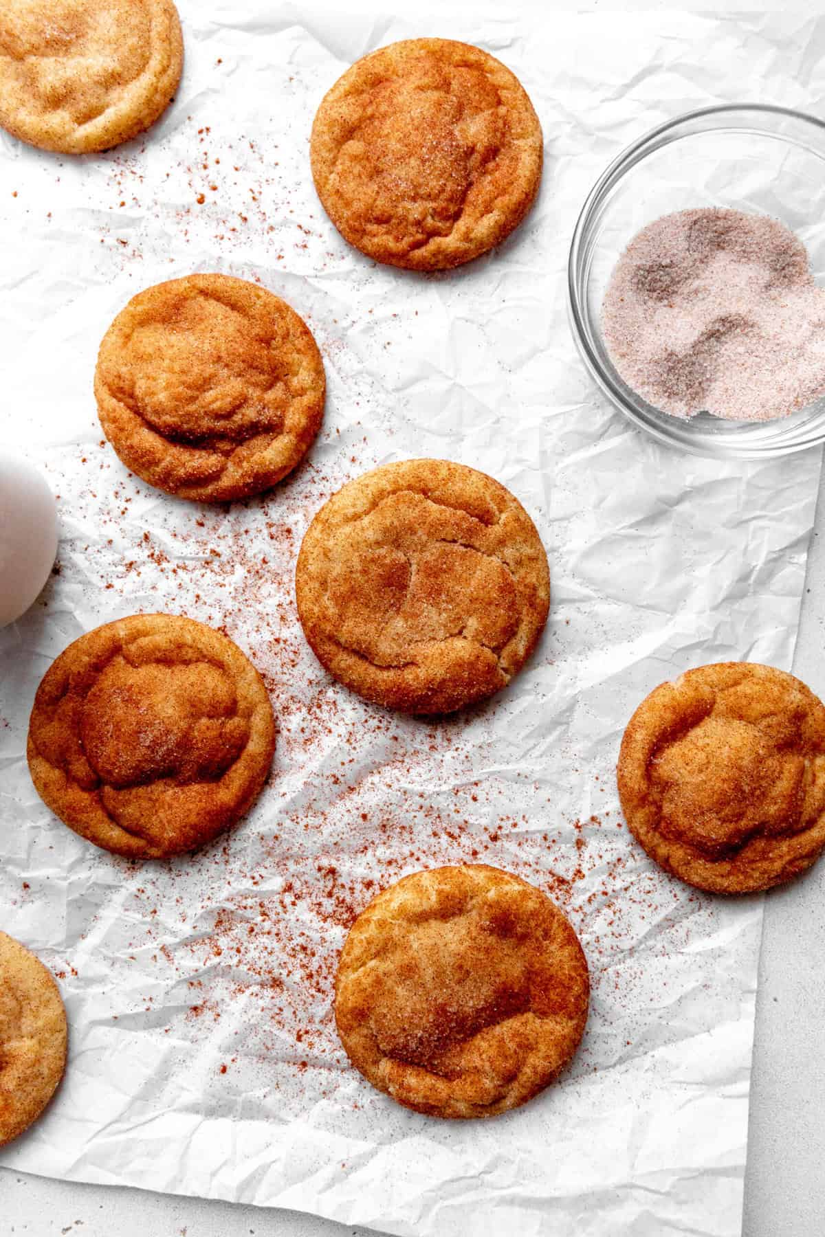 Vegan snickerdoodles spread out on white parchment and a jug of milk.