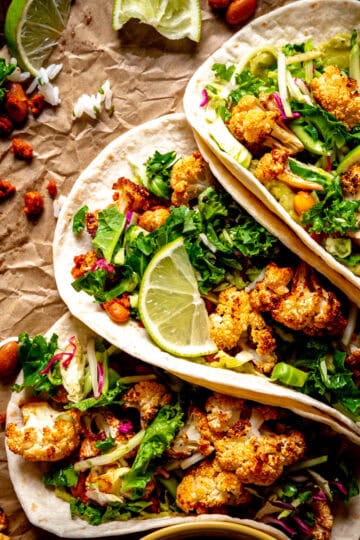Cauliflower tacos filled with beans, slaw and lime wedges.