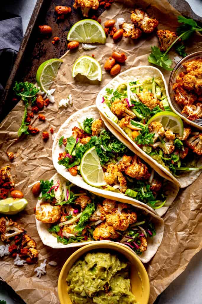 Cauliflower tacos and a cup of guacamole on a baking sheet.