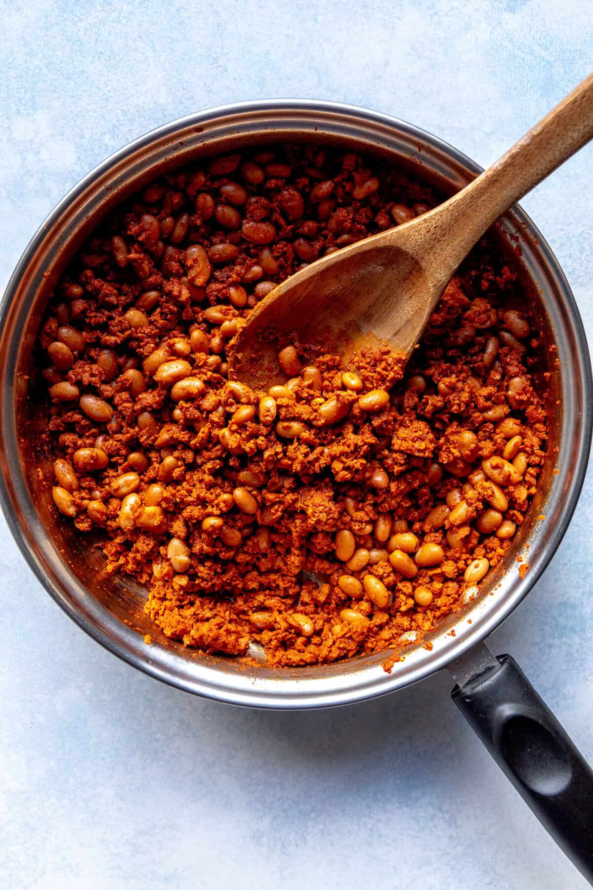 Skillet of soyrizo and beans with a wooden spoon.