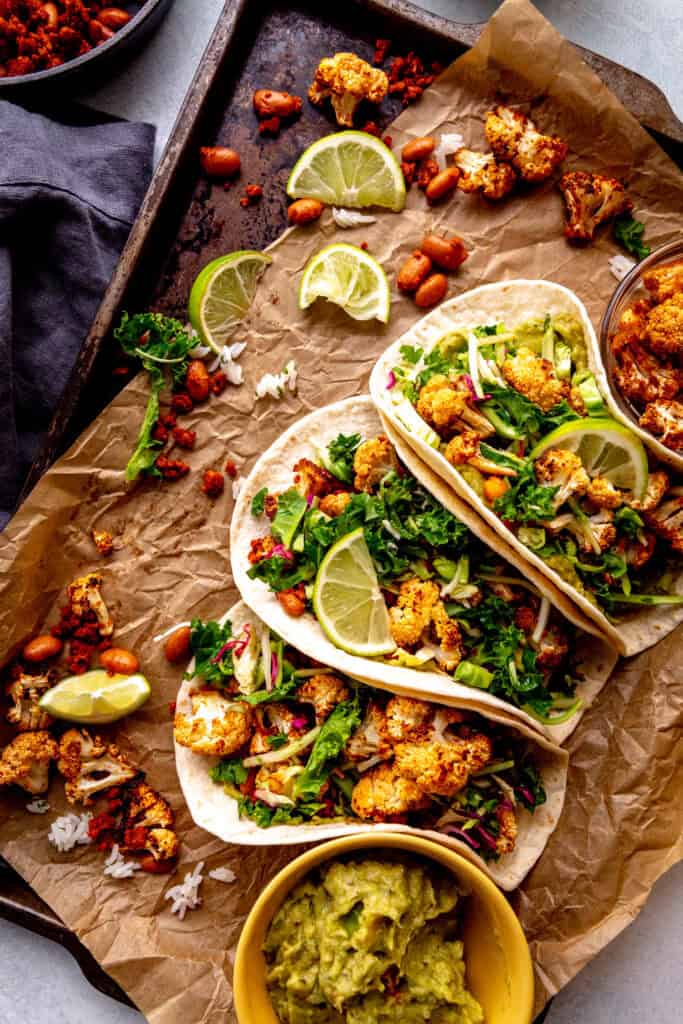 Three cauliflower tacos on a baking sheet with a cup of guacamole.