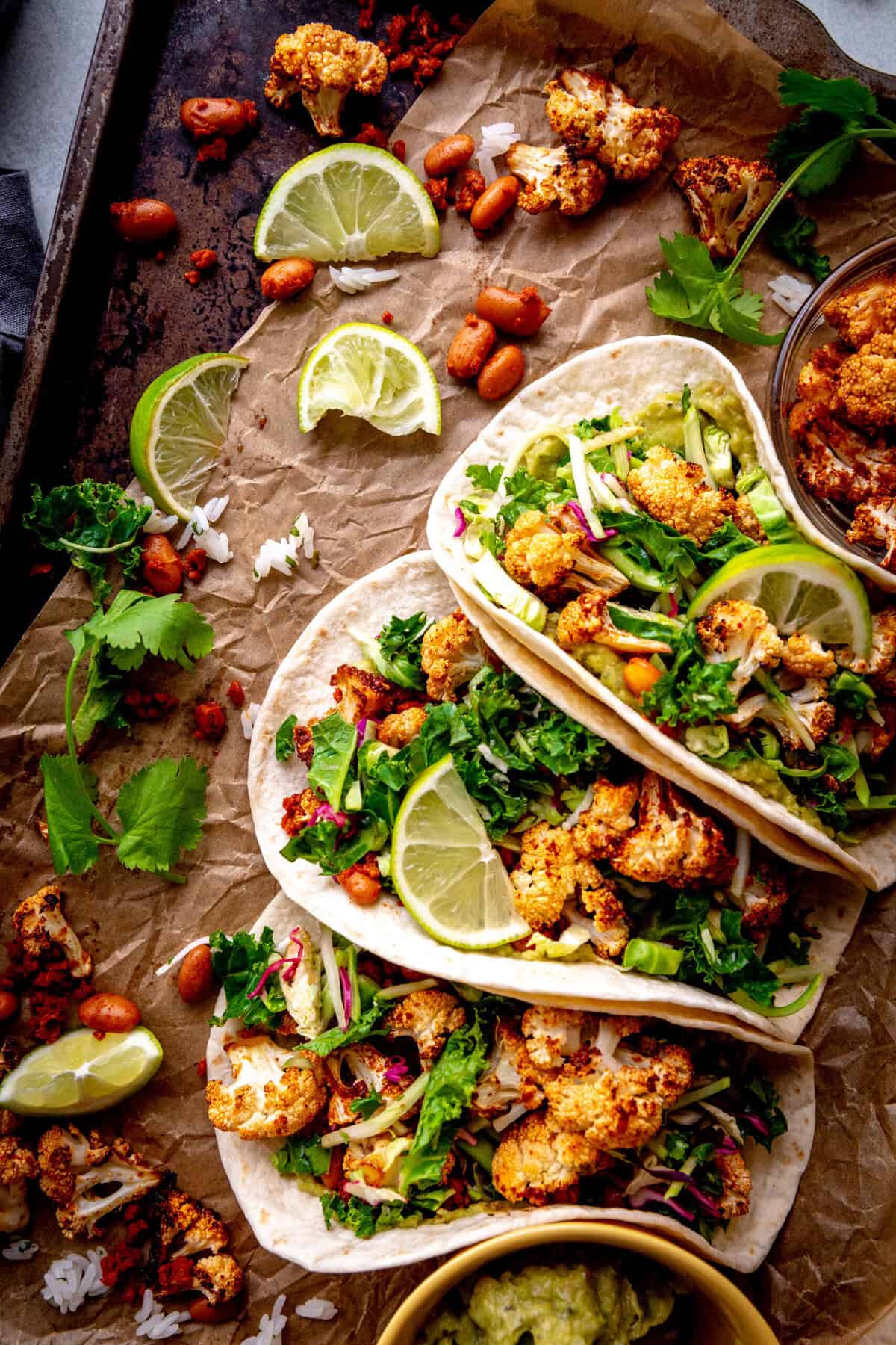 Cauliflower tacos and lime wedges on a baking sheet.