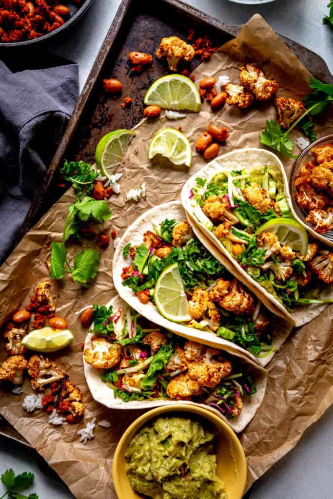 Cauliflower tacos and a cup of guacamole on a baking sheet.
