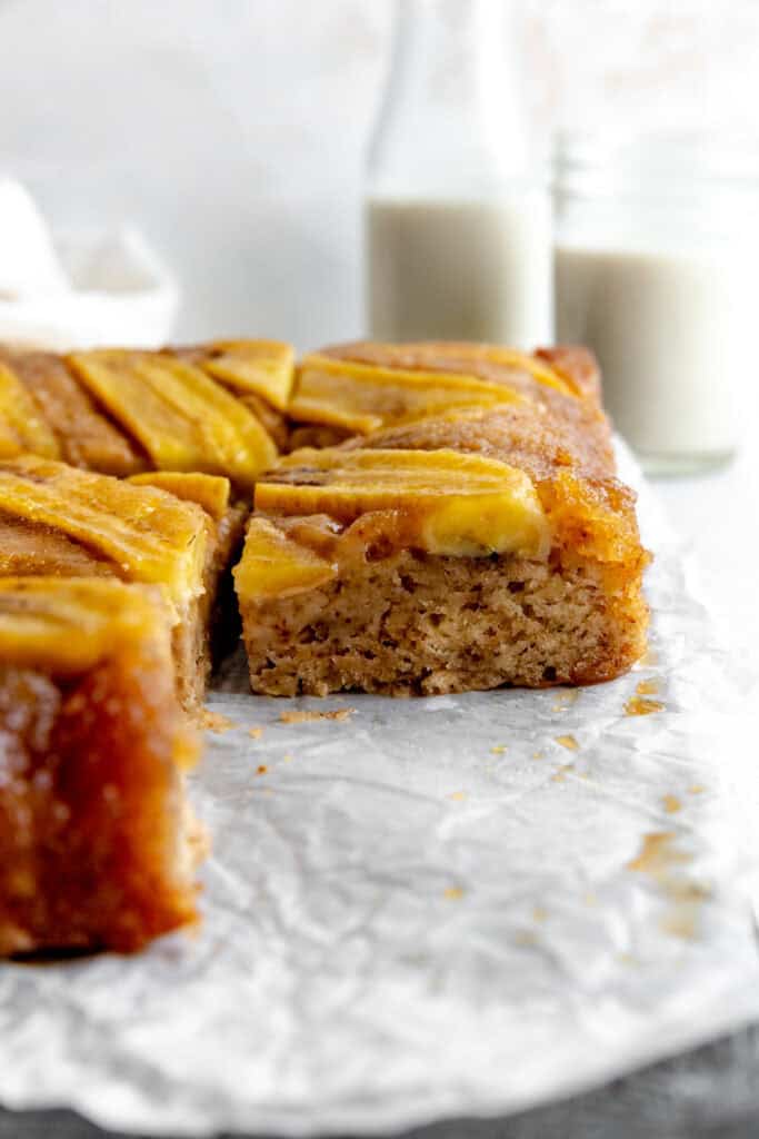Piece of banana upside down cake in front of a jug of milk.