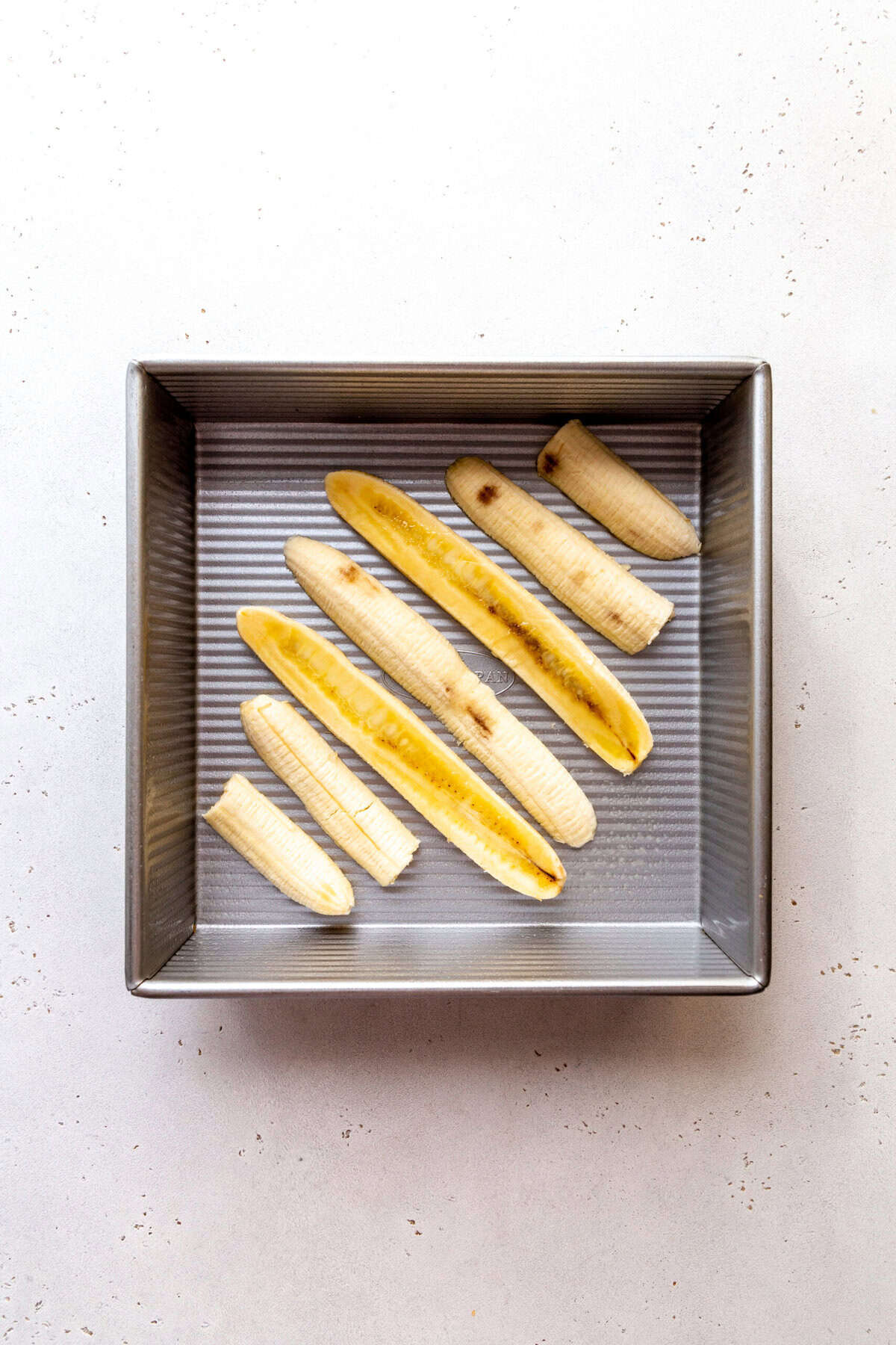 Sliced bananas laid out on a square pan.